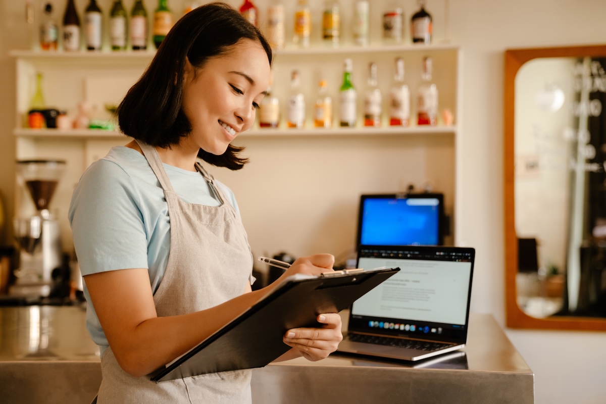 Young barista woman writing down notes while working in cafe